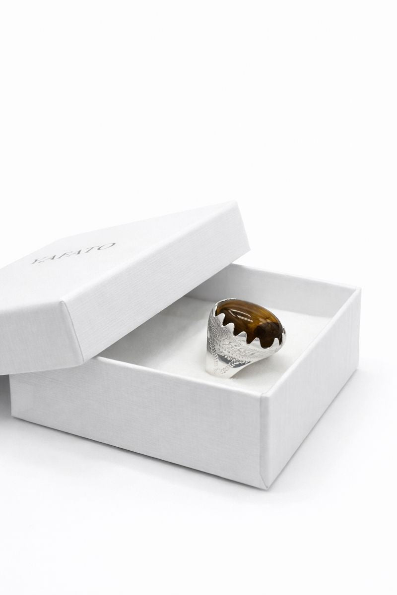 Silver ring with a brown stone in an open white box on a white background
