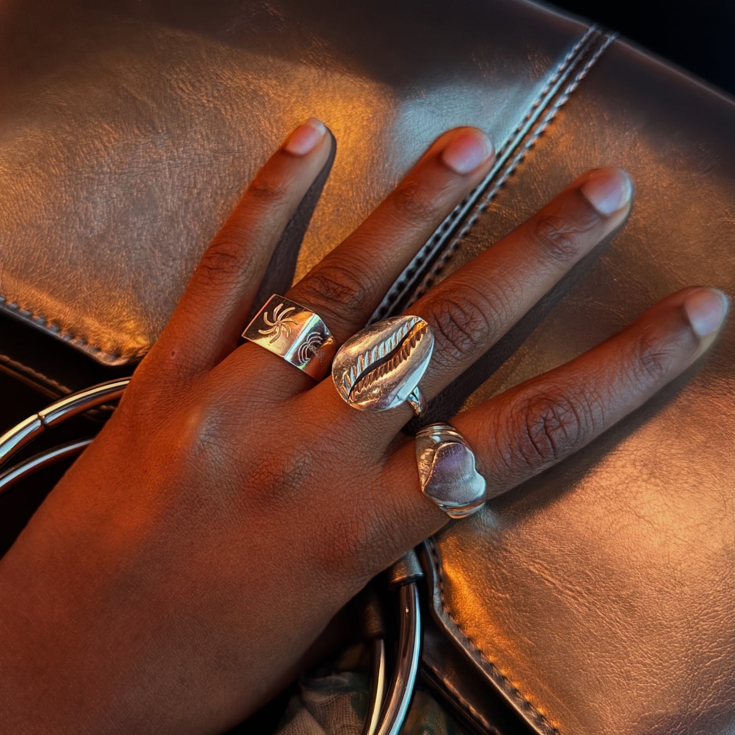 Hand wearing multiple silver rings on a brown leather surface