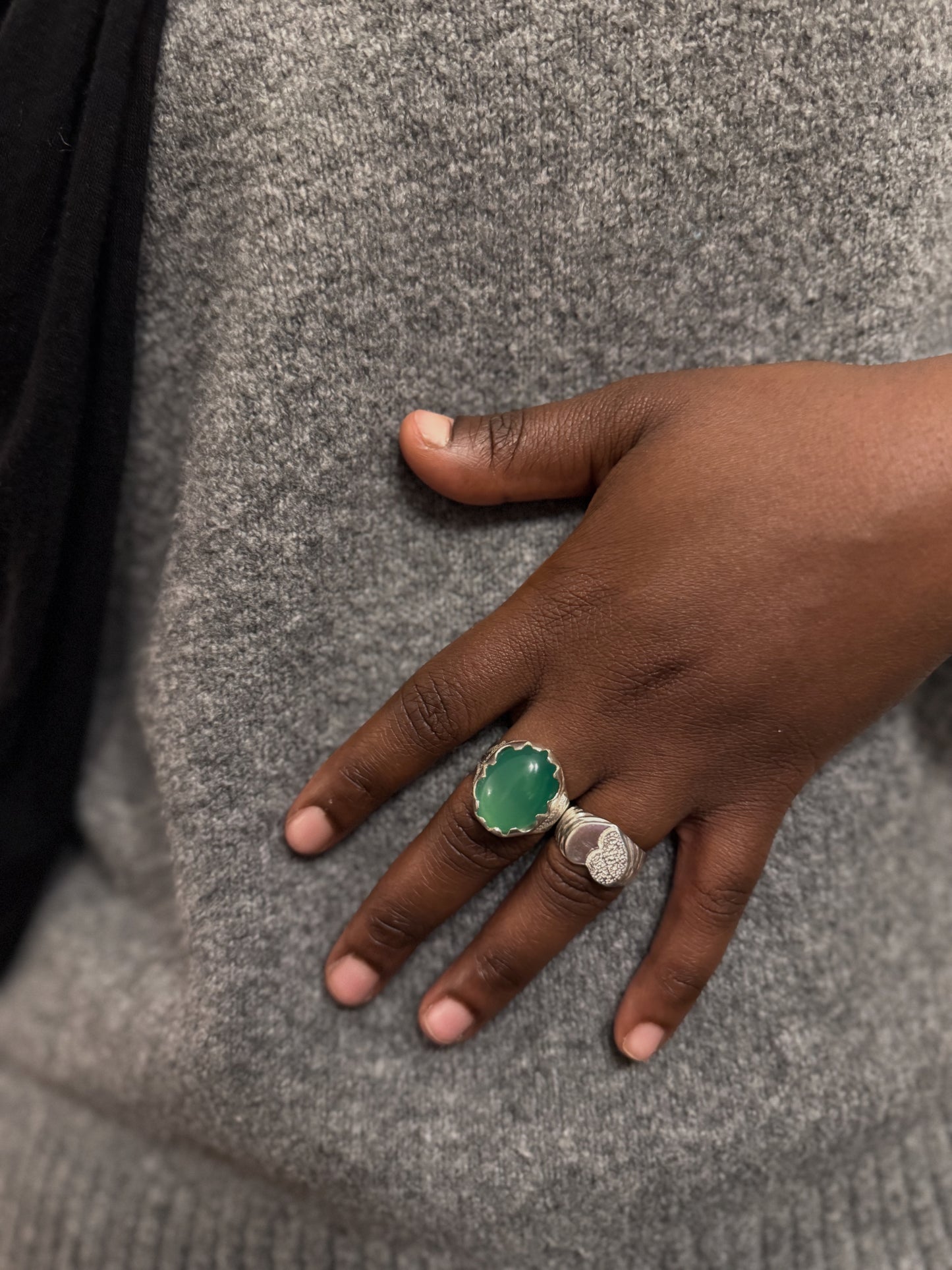 Hand wearing a green ring on a gray textured background
