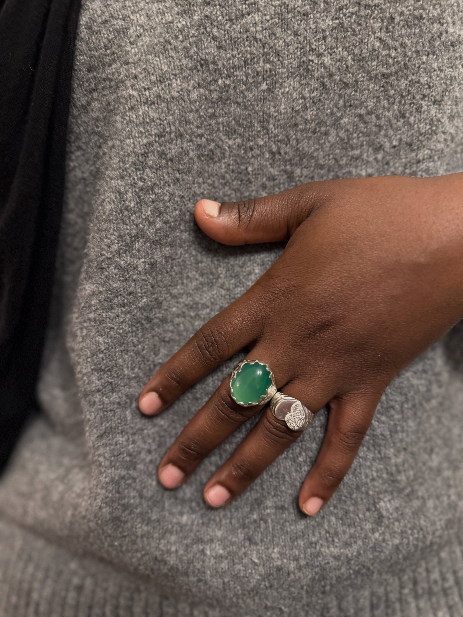 Hand wearing a green ring on a gray textured background