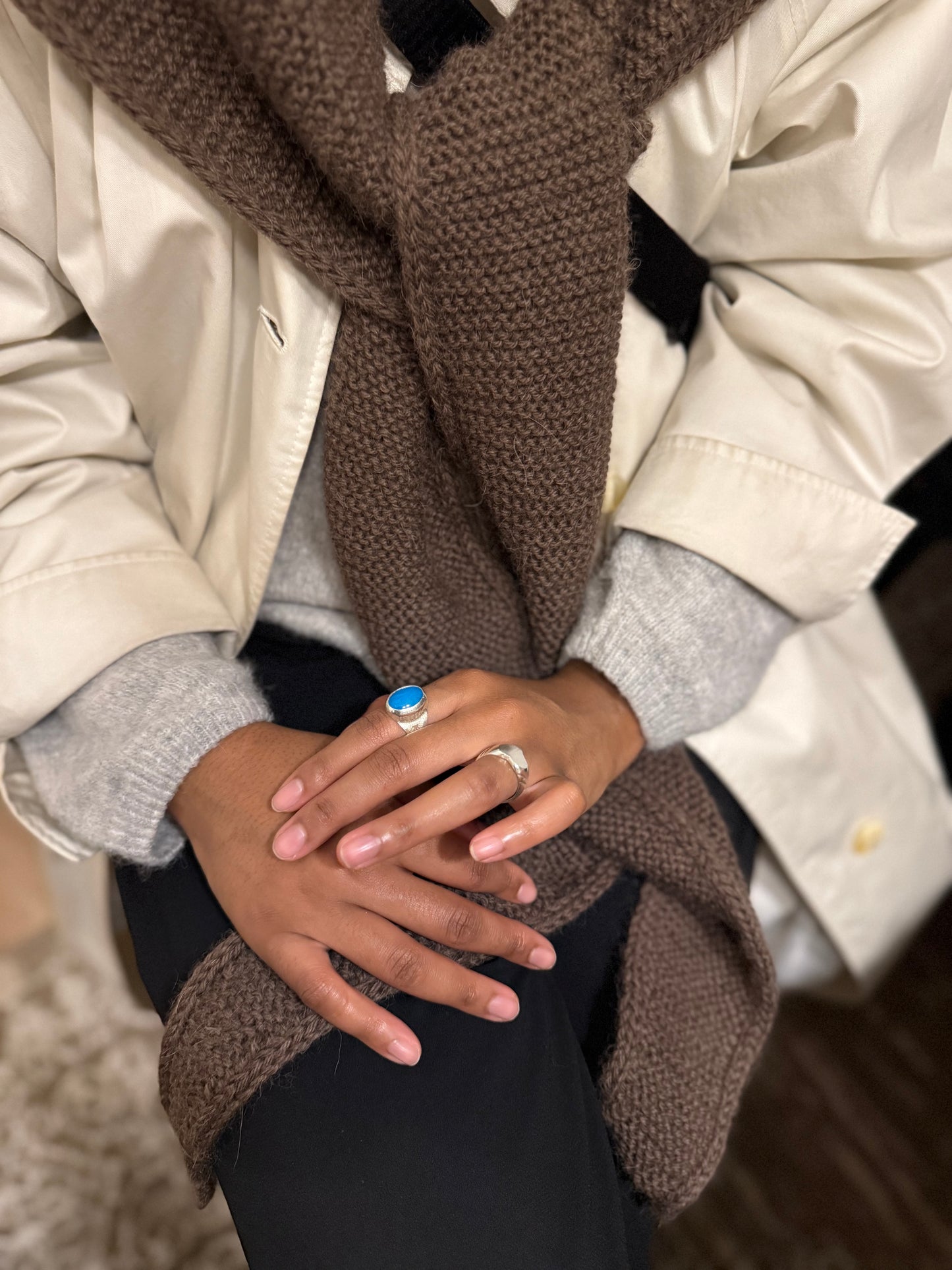 Close-up of hands wearing rings with a brown scarf and beige jacket.
