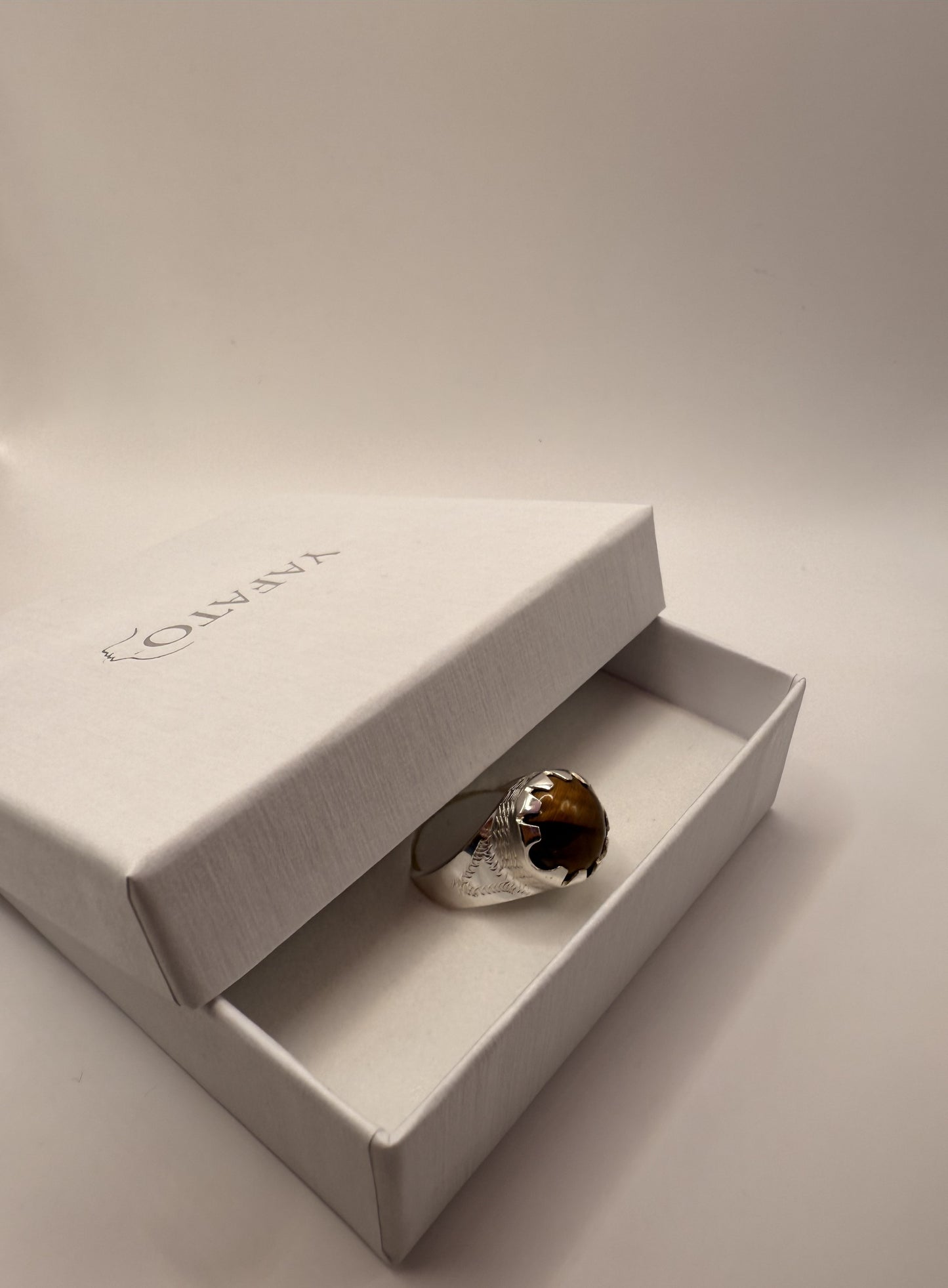 Silver ring with a brown stone in a yafato jewelry box on a light beige background
