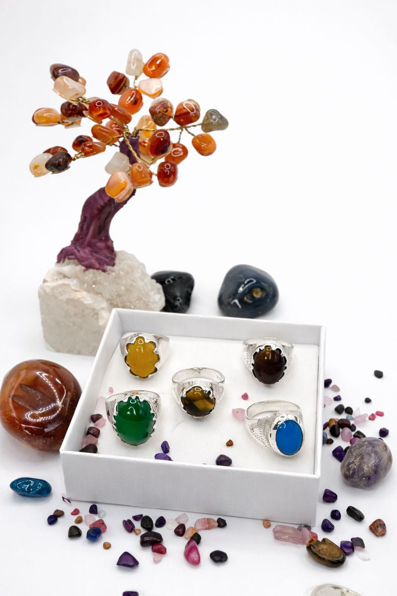 Colorful crystal tree and stones with silver rings displayed on a white background
